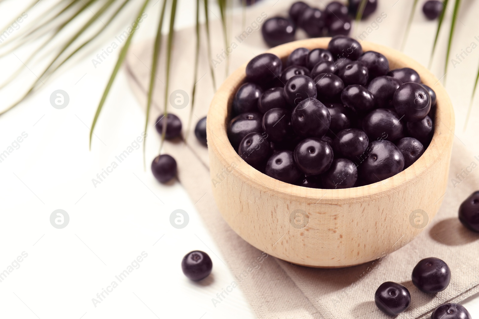 Photo of Ripe acai berries in bowl on white table, closeup. Space for text