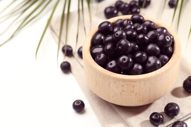 Photo of Ripe acai berries in bowl on white table, closeup. Space for text