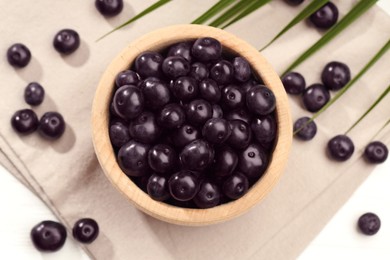 Ripe acai berries in bowl on white table, flat lay