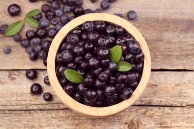 Ripe acai berries and leaves in bowl on wooden table, top view