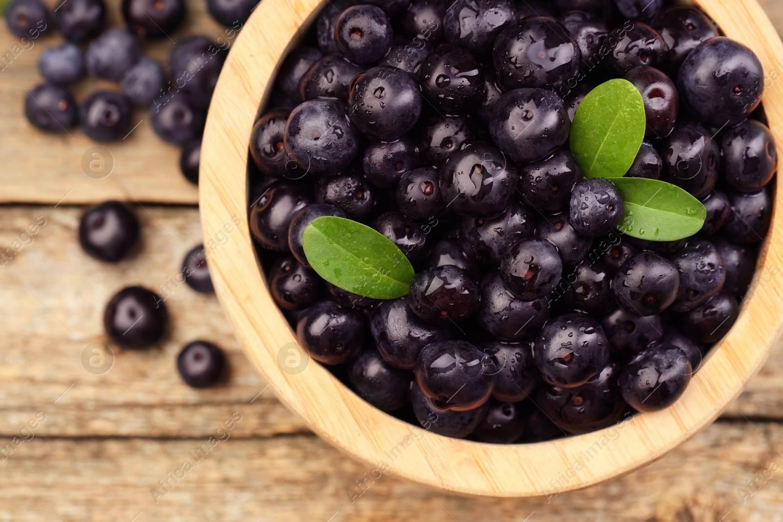 Photo of Ripe acai berries and leaves in bowl on wooden table, top view