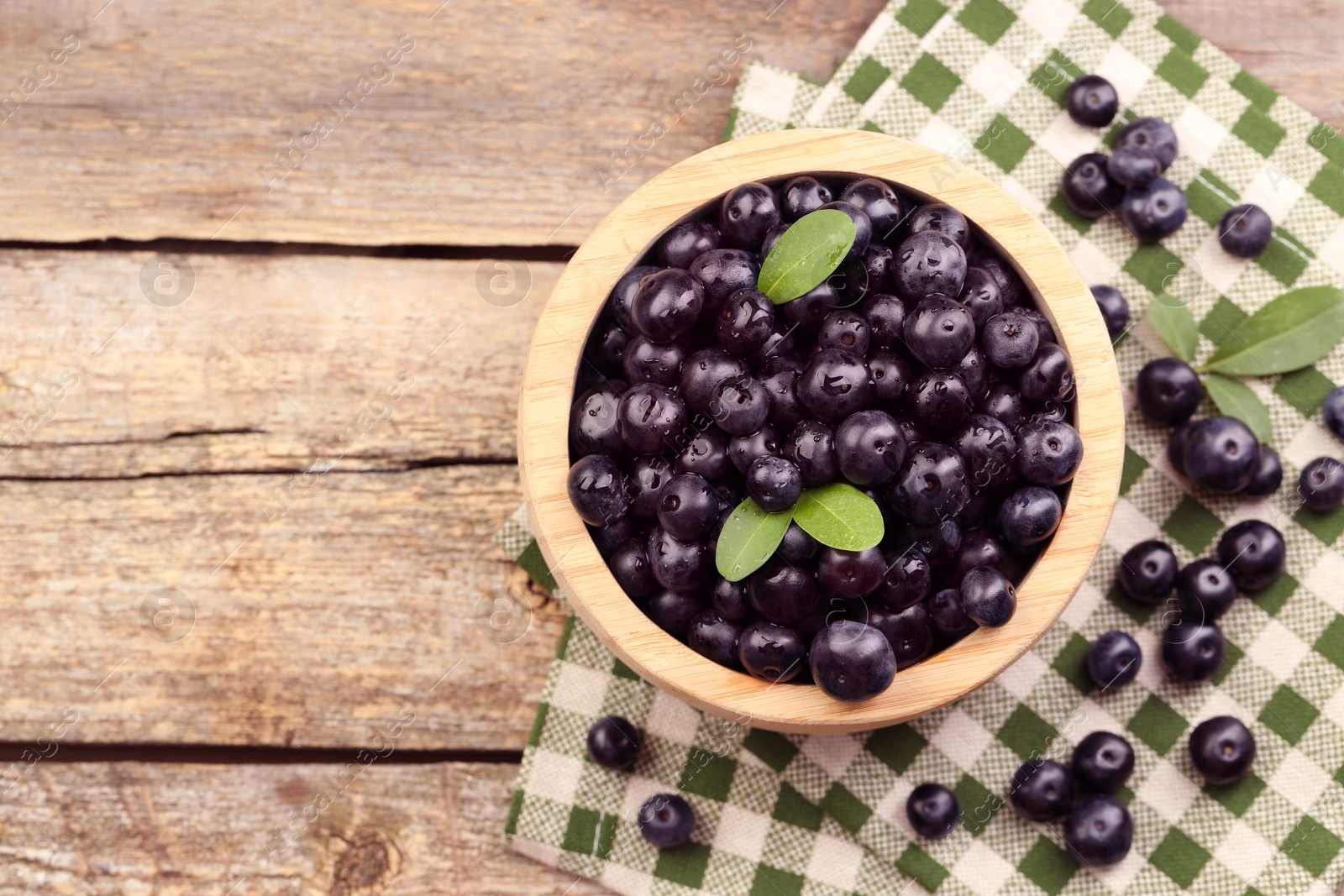 Photo of Ripe acai berries and leaves in bowl on wooden table, top view. Space for text