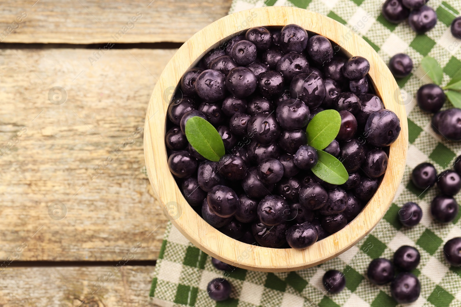 Photo of Ripe acai berries and leaves in bowl on wooden table, top view. Space for text