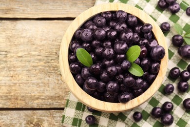 Photo of Ripe acai berries and leaves in bowl on wooden table, top view. Space for text