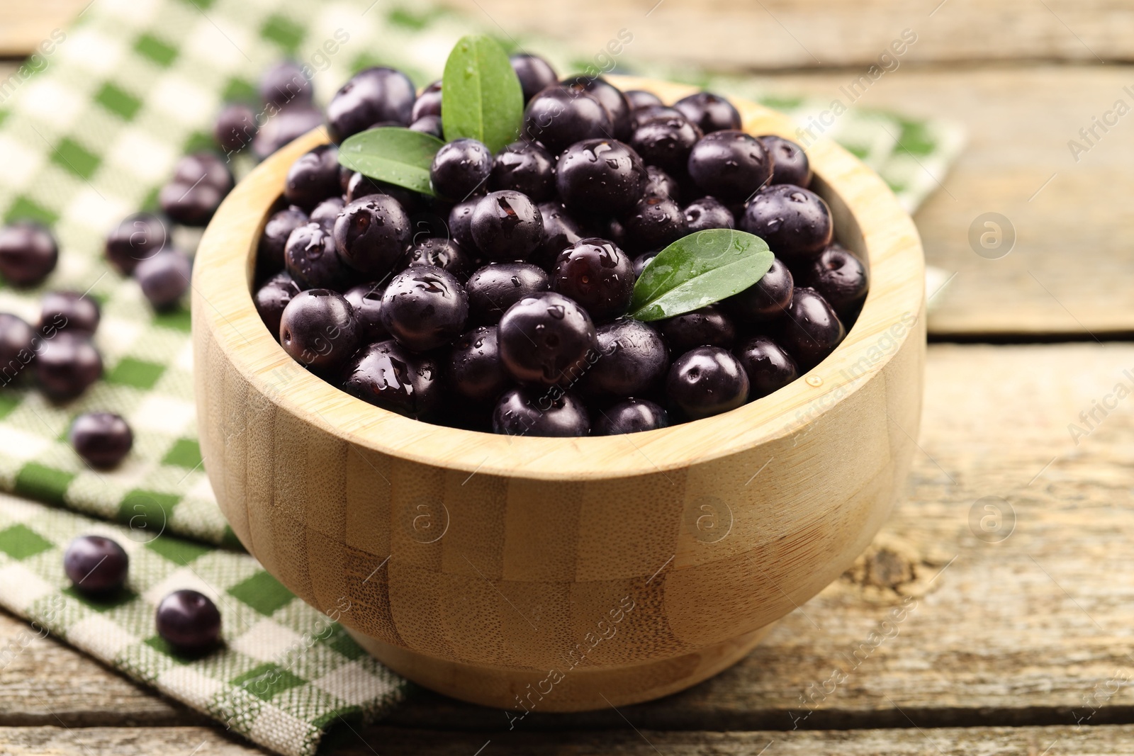 Photo of Ripe acai berries and leaves in bowl on wooden table, closeup