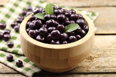 Ripe acai berries and leaves in bowl on wooden table, closeup