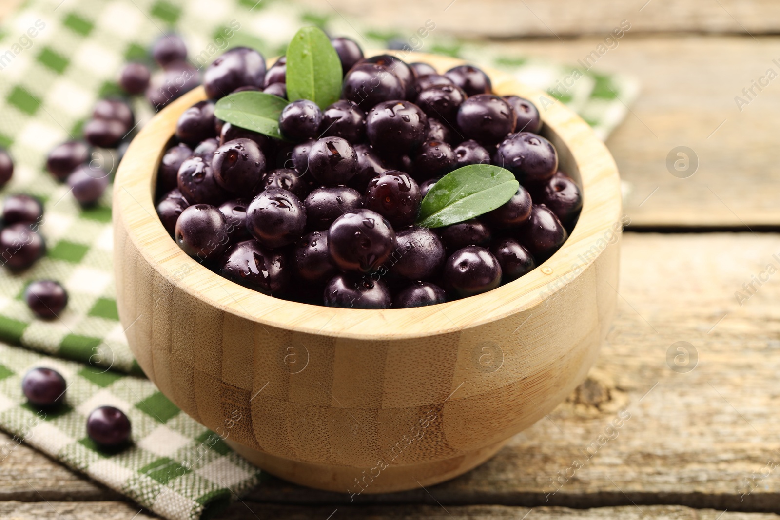 Photo of Ripe acai berries and leaves in bowl on wooden table, closeup