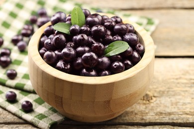 Photo of Ripe acai berries and leaves in bowl on wooden table, closeup