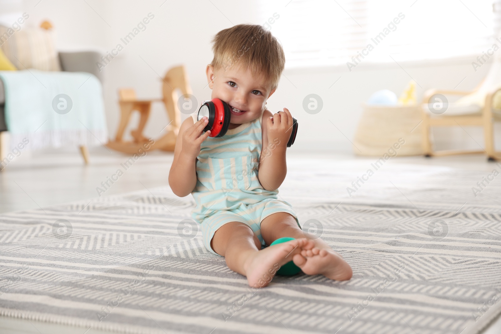 Photo of Cute little baby with headphones on floor at home