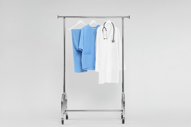 Photo of Different medical workers' uniforms and stethoscope on clothing rack against white background