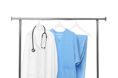 Photo of Different medical workers' uniforms and stethoscope on clothing rack against white background