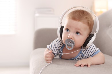 Cute little baby with headphones and pacifier on sofa at home, space for text