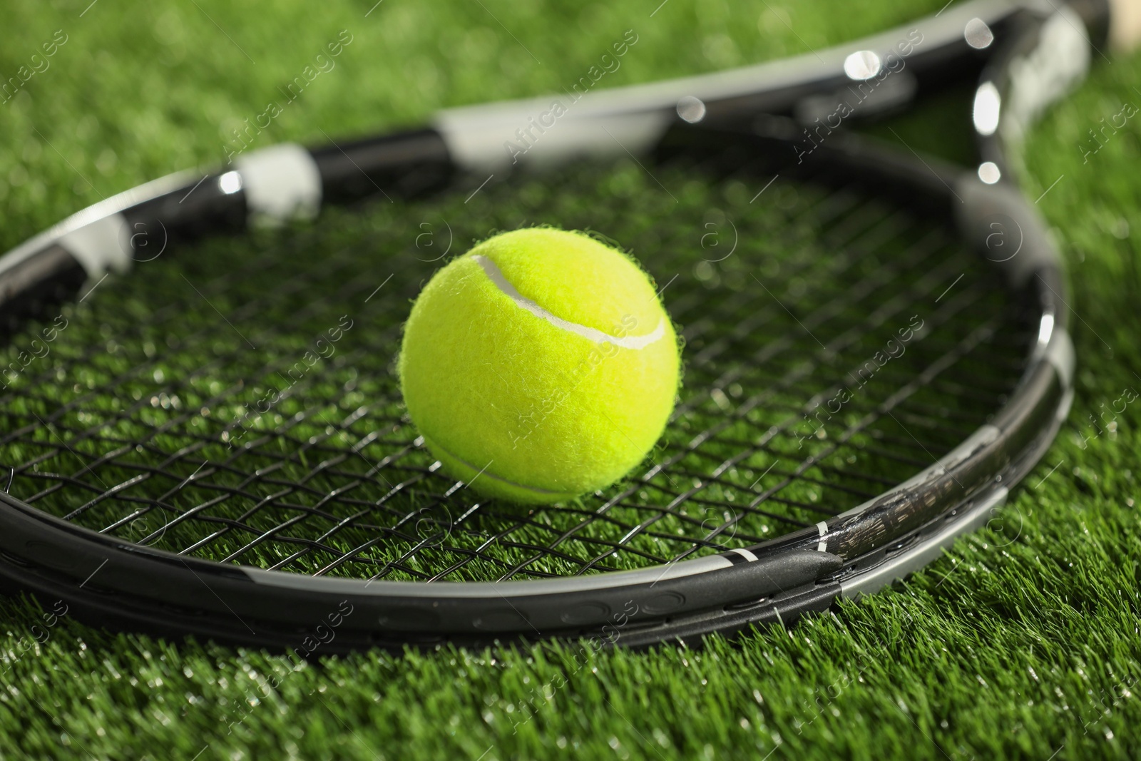 Photo of Tennis racket and ball on green grass, closeup