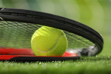 Photo of Tennis racket and ball on green artificial grass, closeup