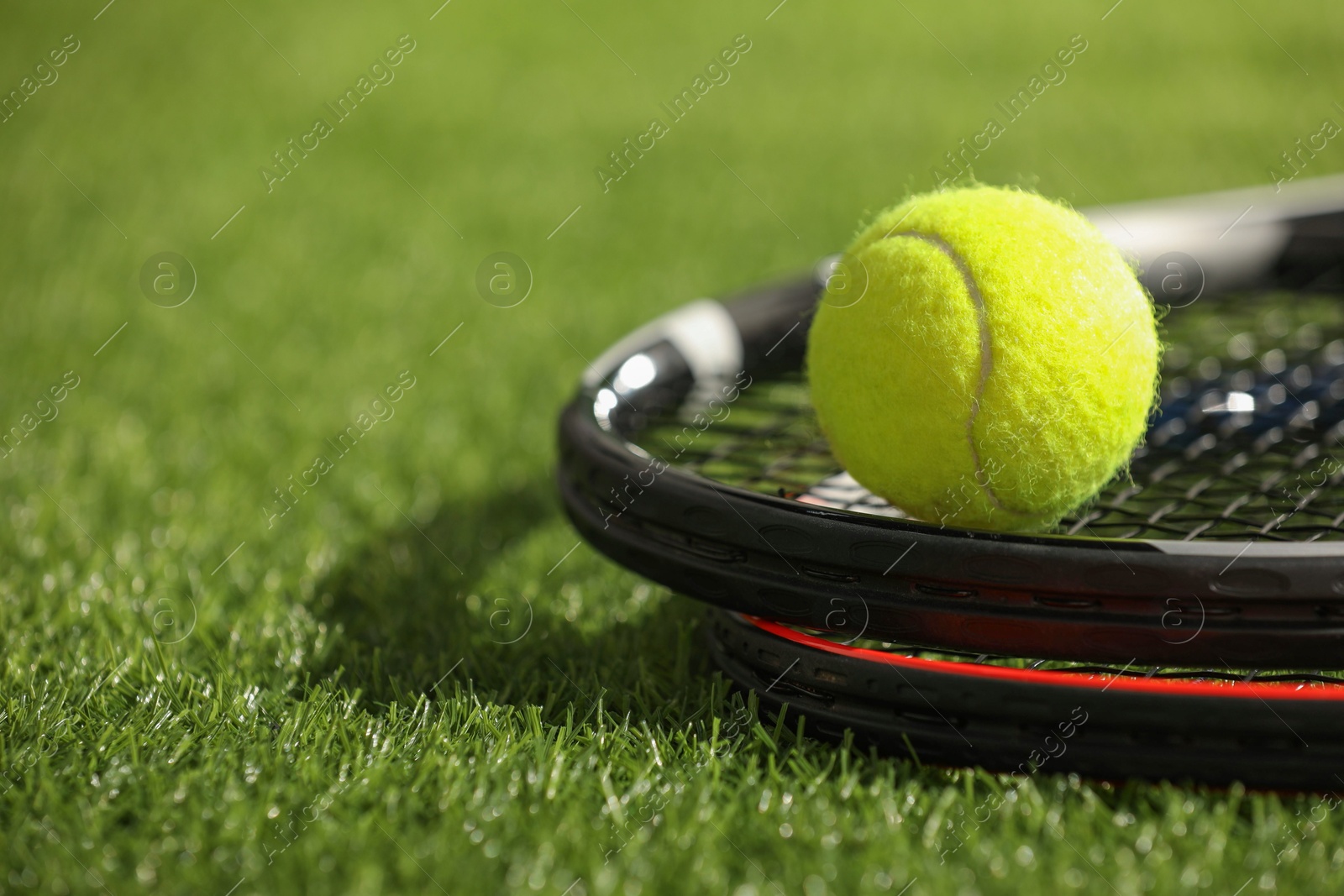 Photo of Tennis rackets and ball on green artificial grass, closeup. Space for text