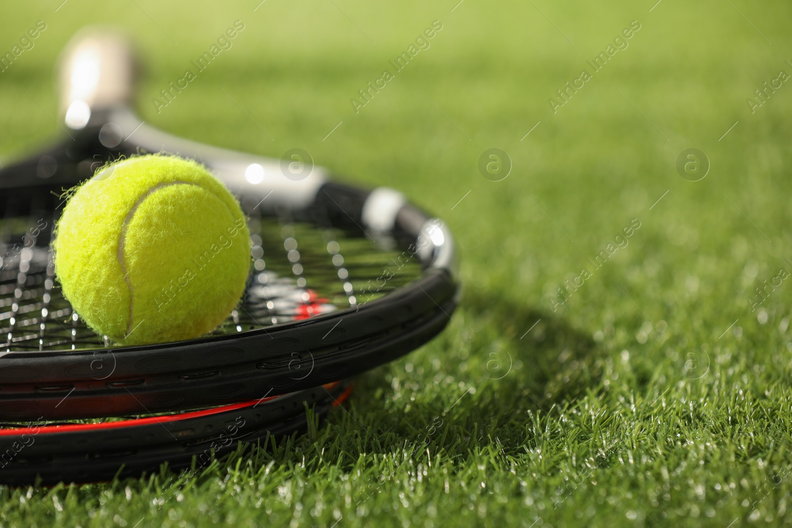 Photo of Tennis rackets and ball on green artificial grass, closeup. Space for text