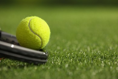 Photo of Tennis racket and ball on green artificial grass, closeup. Space for text