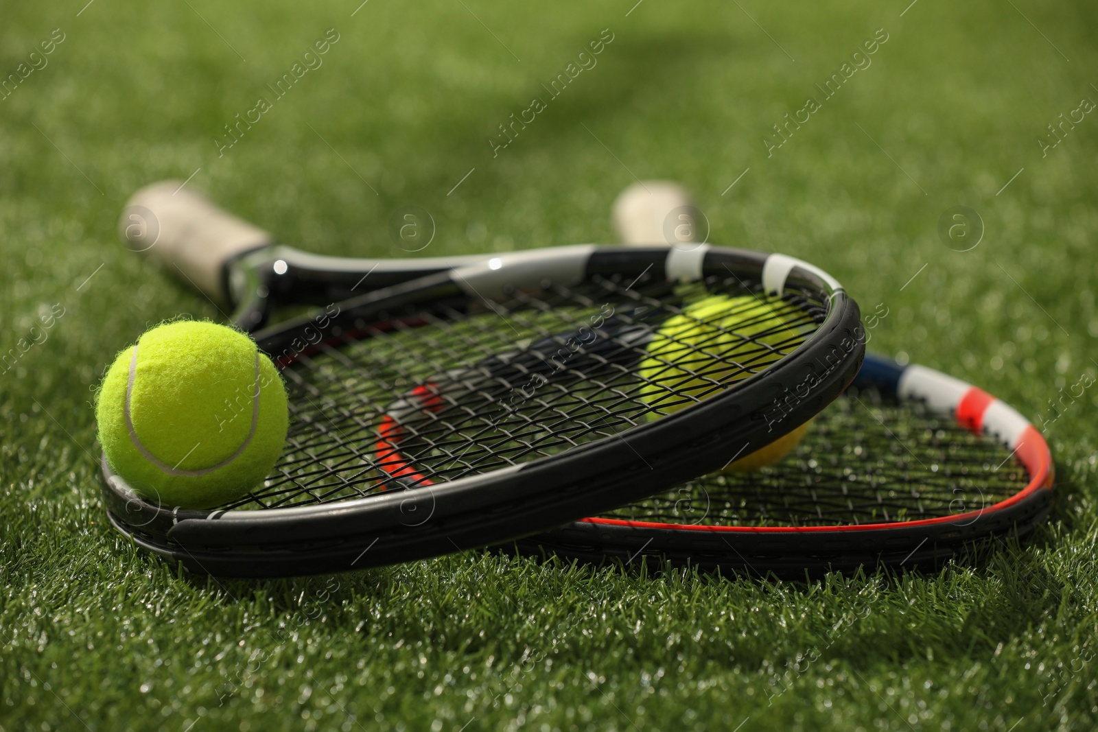 Photo of Tennis rackets and balls on green artificial grass, closeup