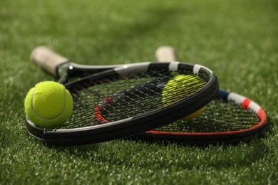 Photo of Tennis rackets and balls on green artificial grass, closeup