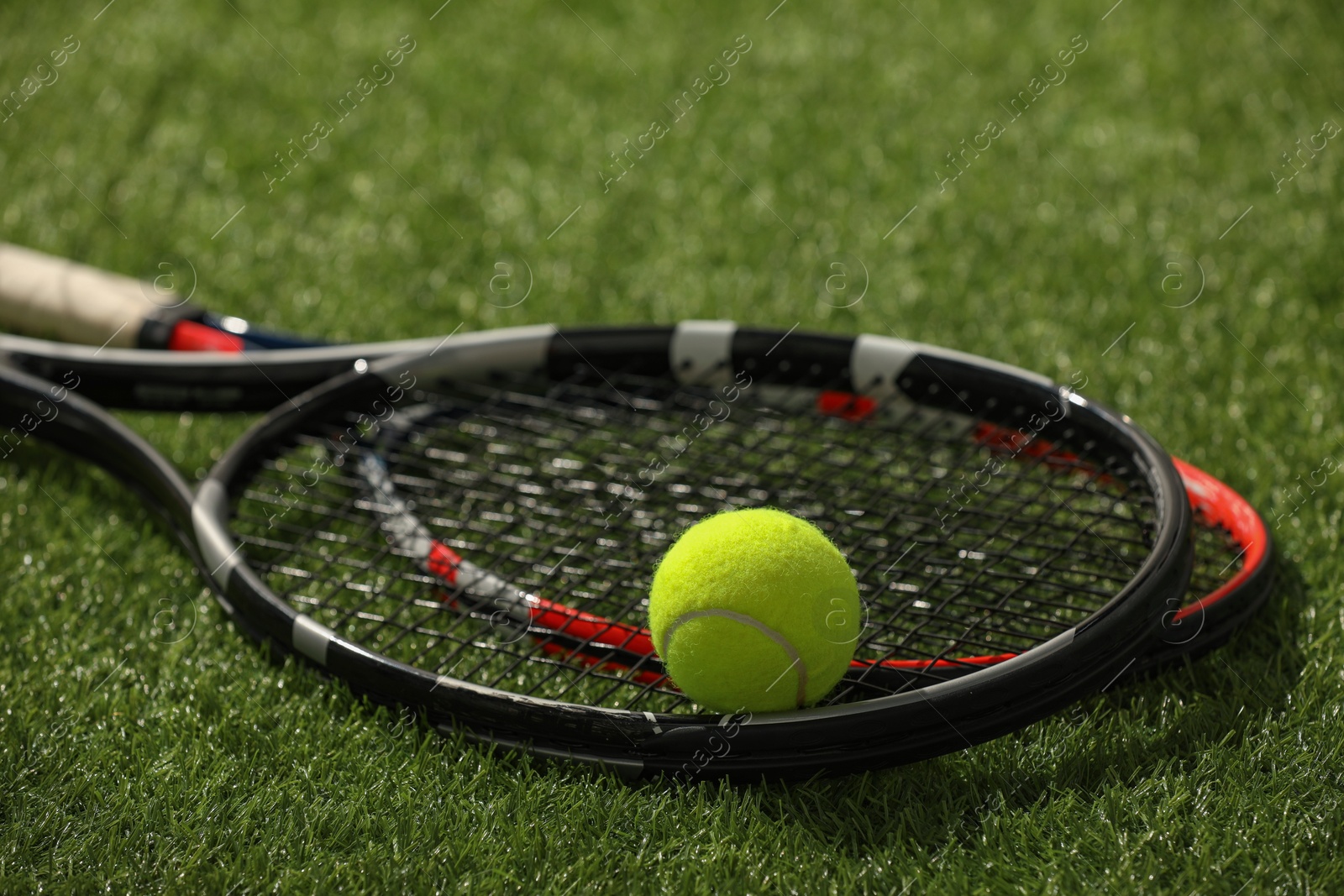 Photo of Tennis rackets and ball on green artificial grass, closeup