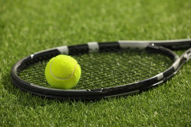 Photo of Tennis racket and ball on green artificial grass, closeup