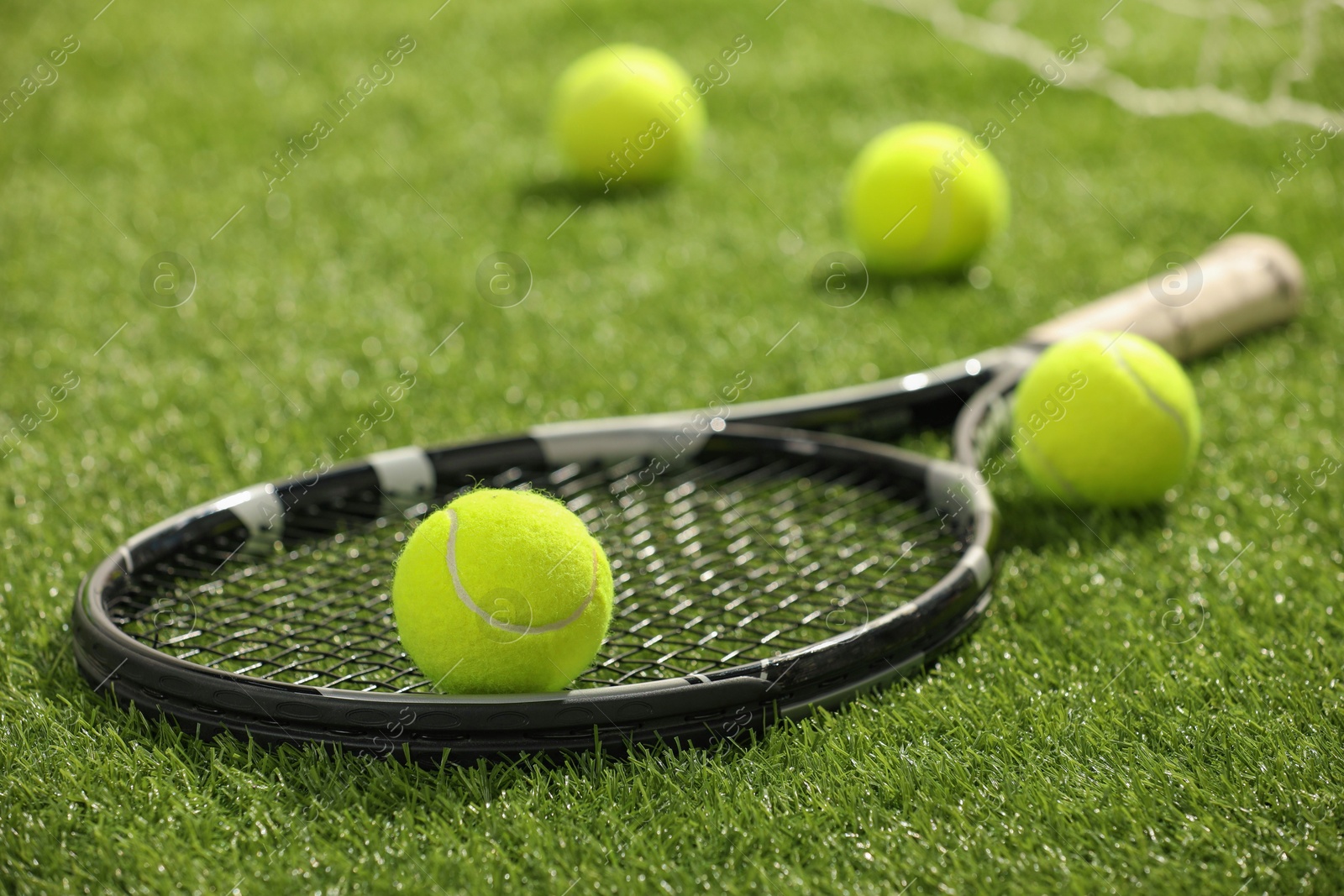 Photo of Tennis racket and balls on green artificial grass, closeup