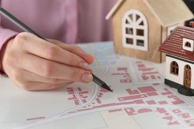 Photo of House hunting. Woman with maps and house figures at table, closeup