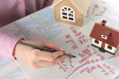 Photo of House hunting. Woman with maps and house figures at table, closeup