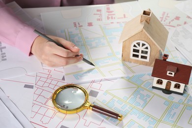 Photo of House hunting. Woman with maps, magnifying glass and house figures at white table, closeup