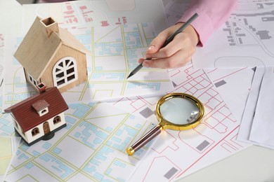 Photo of House hunting. Woman with maps, magnifying glass and house figures at white table, closeup