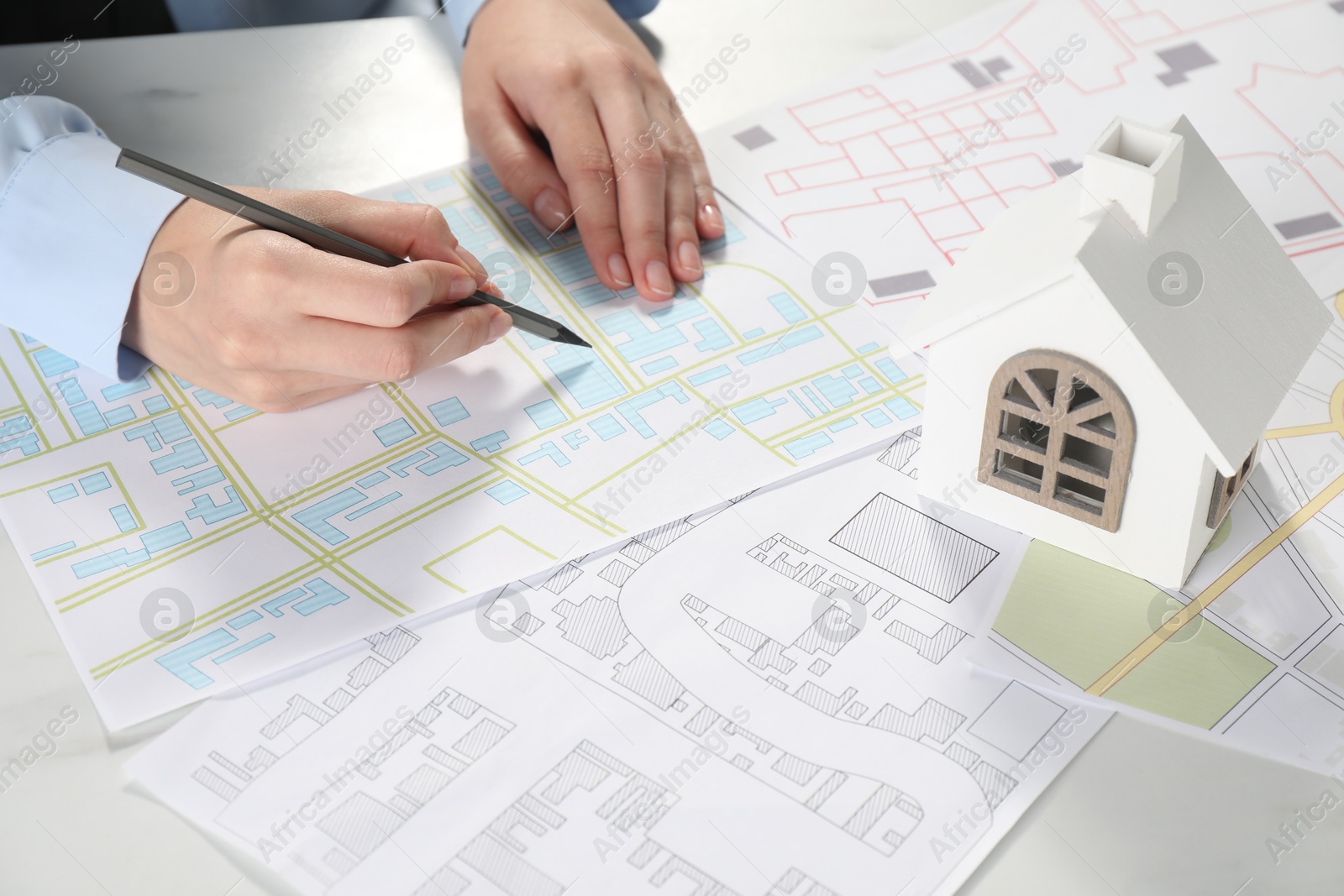 Photo of House hunting. Woman with maps and house figure at white table, closeup