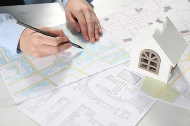 Photo of House hunting. Woman with maps and house figure at white table, closeup