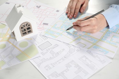 Photo of House hunting. Woman with maps and house figure at white table, closeup