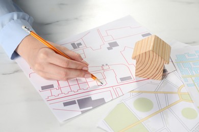 House hunting. Woman with maps and house figure at white marble table, closeup