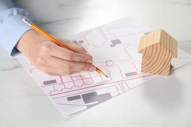 House hunting. Woman with maps and house figure at white marble table, closeup