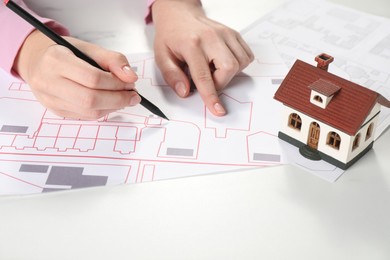 House hunting. Woman with maps and house figure at white table, closeup