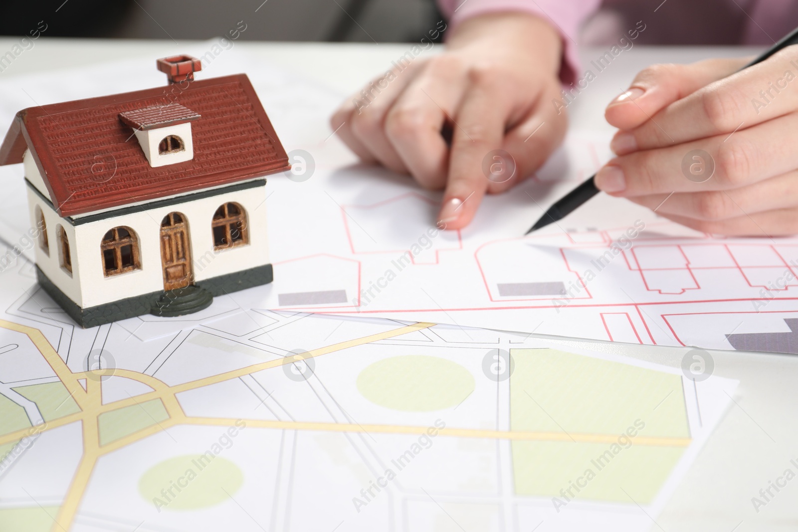 Photo of House hunting. Woman with maps and house figure at white table, closeup