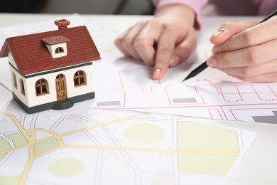 House hunting. Woman with maps and house figure at white table, closeup