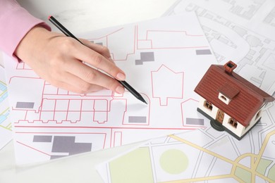 Photo of House hunting. Woman with maps and house figure at white table, closeup