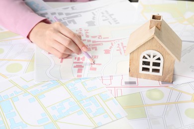 Photo of House hunting. Woman with maps and house figure at white table, closeup