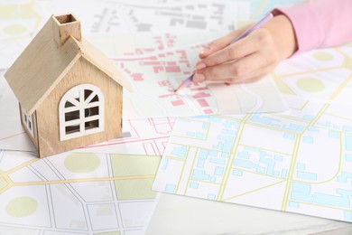 House hunting. Woman with maps and house figure at white table, closeup