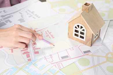 House hunting. Woman with maps and house figure at white table, closeup