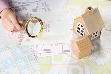 Photo of House hunting. Woman with maps, magnifying glass and house figures at table, closeup