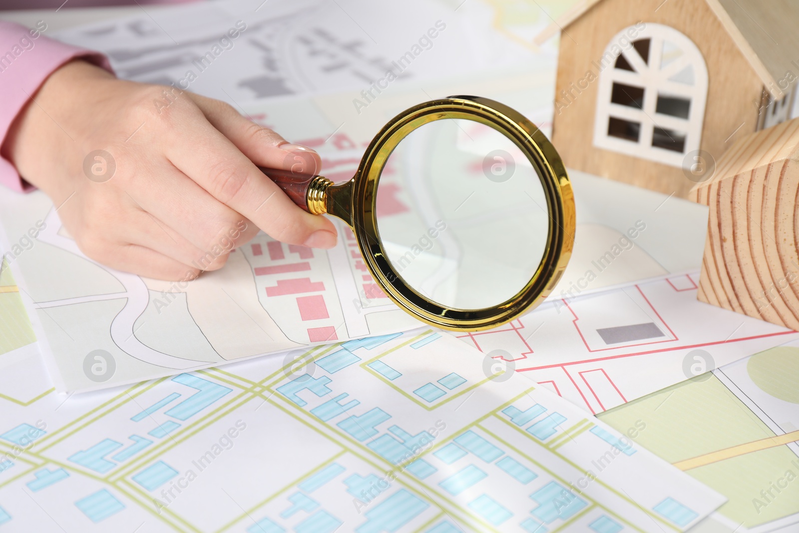 Photo of House hunting. Woman with maps, magnifying glass and house figures at table, closeup