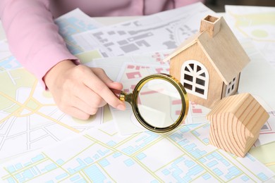 House hunting. Woman with maps, magnifying glass and house figures at table, closeup