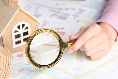 House hunting. Woman with maps, magnifying glass and house figures at table, closeup