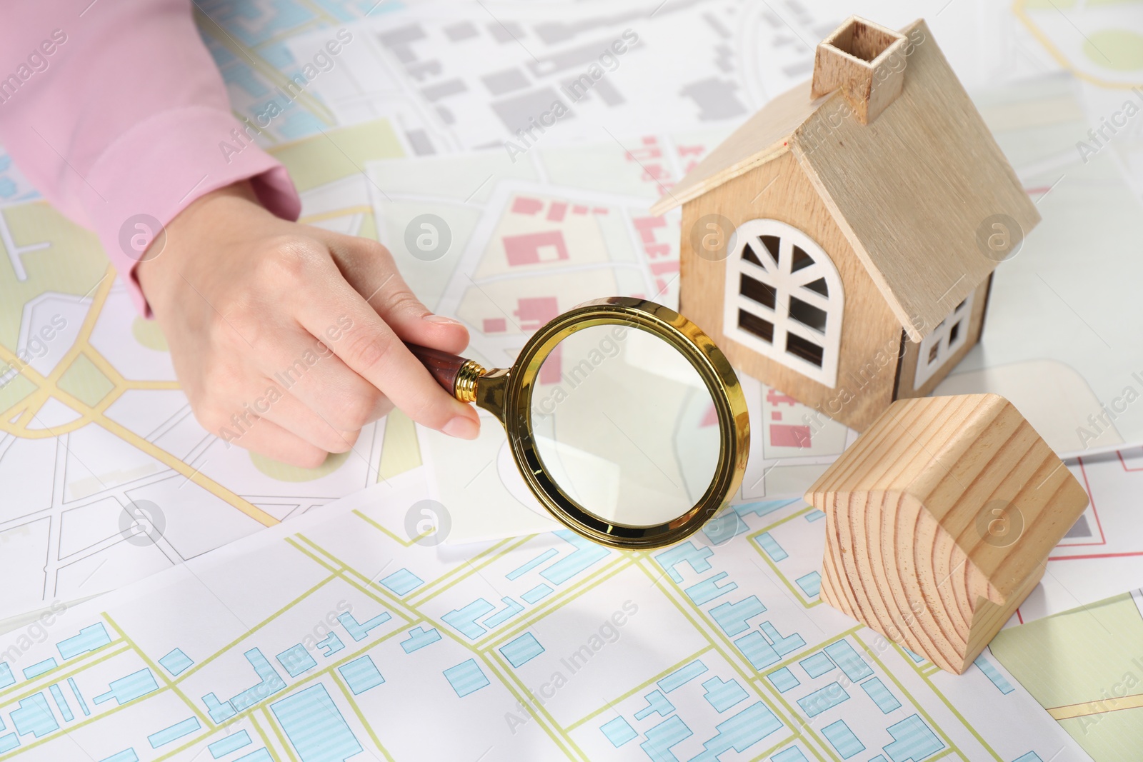 Photo of House hunting. Woman with maps, magnifying glass and house figures at table, closeup