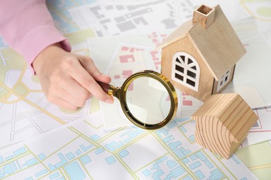 Photo of House hunting. Woman with maps, magnifying glass and house figures at table, closeup