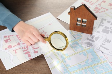 Photo of House hunting. Woman with maps, magnifying glass and house figure at wooden table, closeup