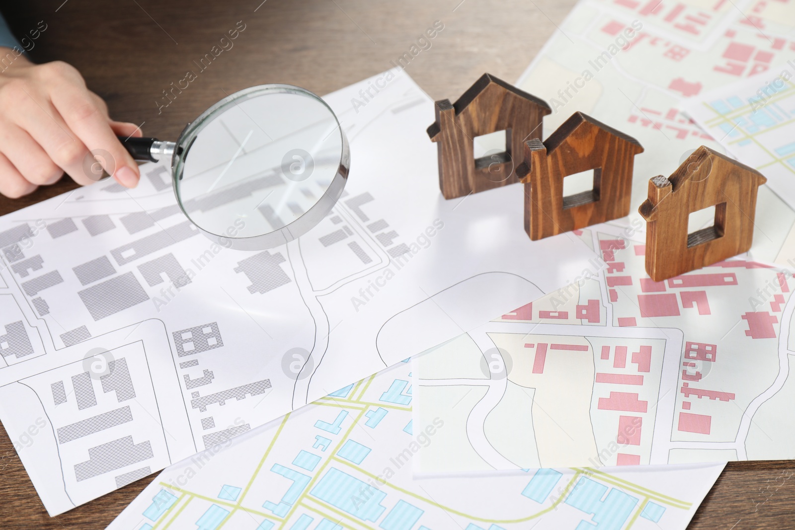 Photo of House hunting. Woman with maps, magnifying glass and house figures at wooden table, closeup